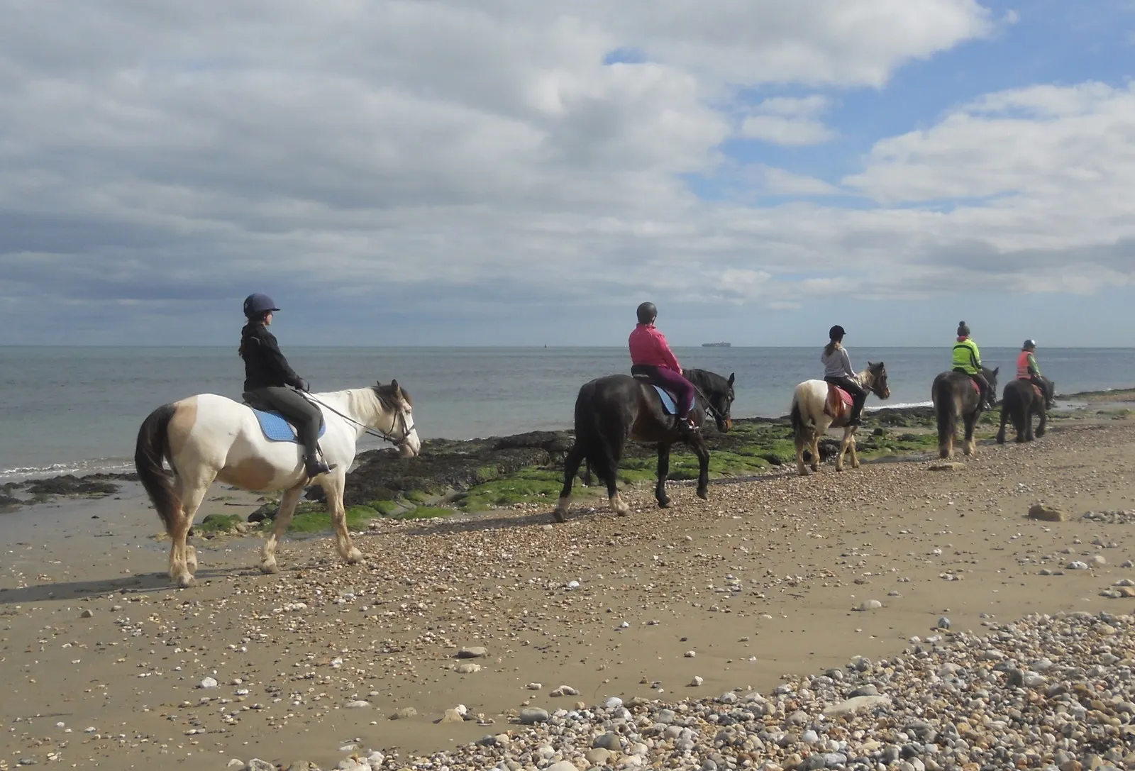 Helmeted riders on horseback along Bembridge beach, England, illustrative image